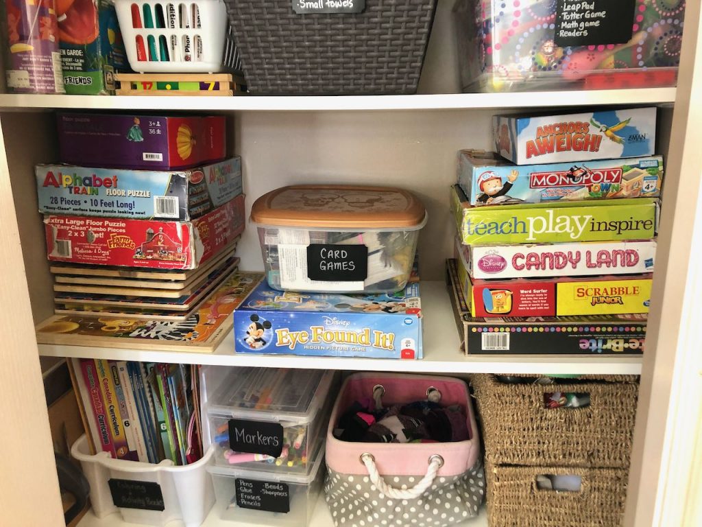 Two closet shelves with bins of games and kids activities