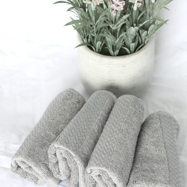 Four grey facecloths rolled up in a row in front of lavender flowers