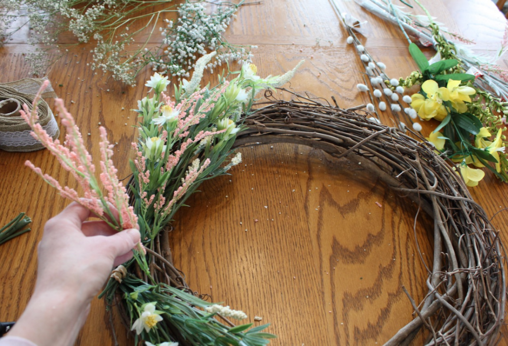Hand attaching coral flower stems onto a grapevine wreath