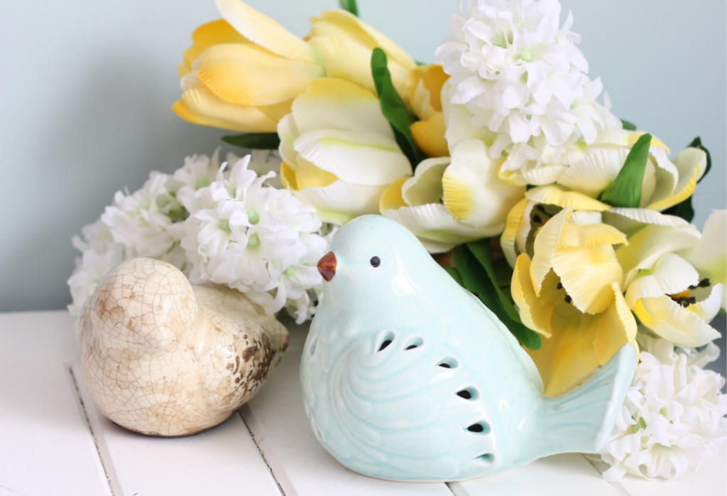Blue and cream bird ornaments beside yellow and white flowers
